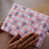 Hand holding a pink checkered box with floral patterns on a blurred background