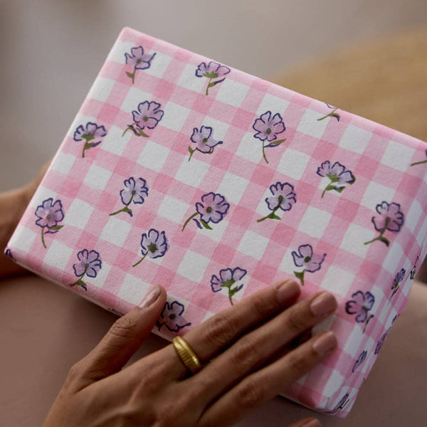 Hand holding a pink checkered box with floral patterns on a blurred background