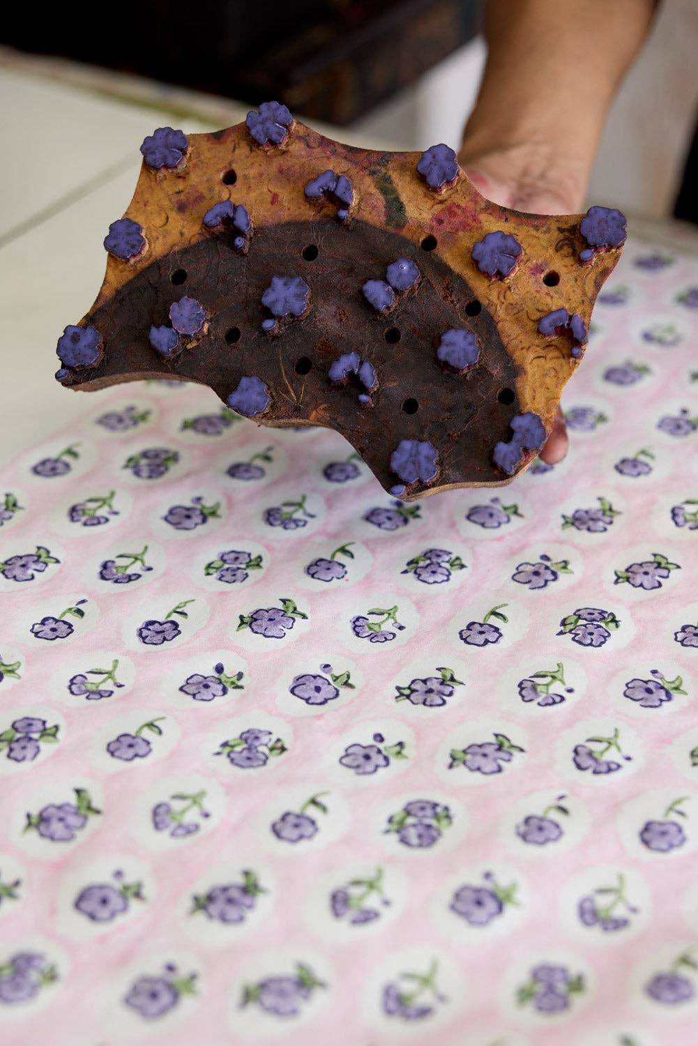Person holding a star-shaped cookie with purple toppings on a pink floral fabric background