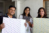 Three people holding fabric swatches with floral patterns indoors.