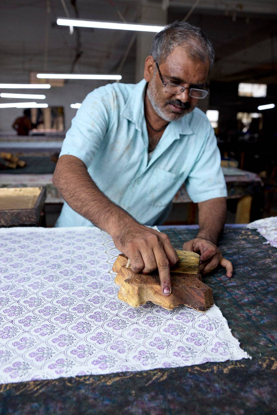 Man working with fabric and a wooden tool in a workshop setting