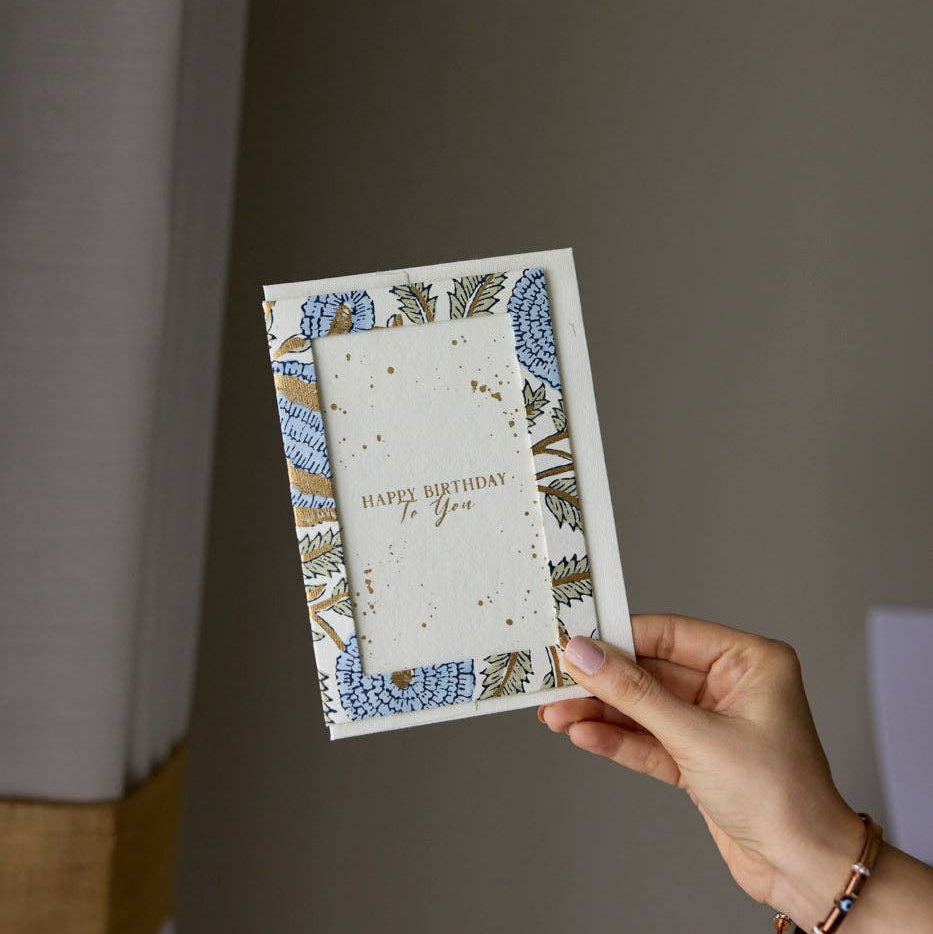 Hand holding a birthday card with decorative border against a plain background
