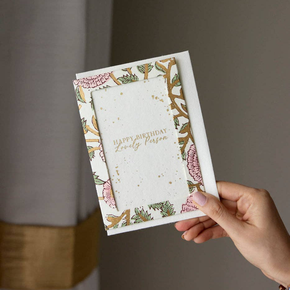 Hand holding a floral birthday card against a neutral background
