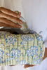 Hand holding a glass of water with a floral-patterned fabric pouch.