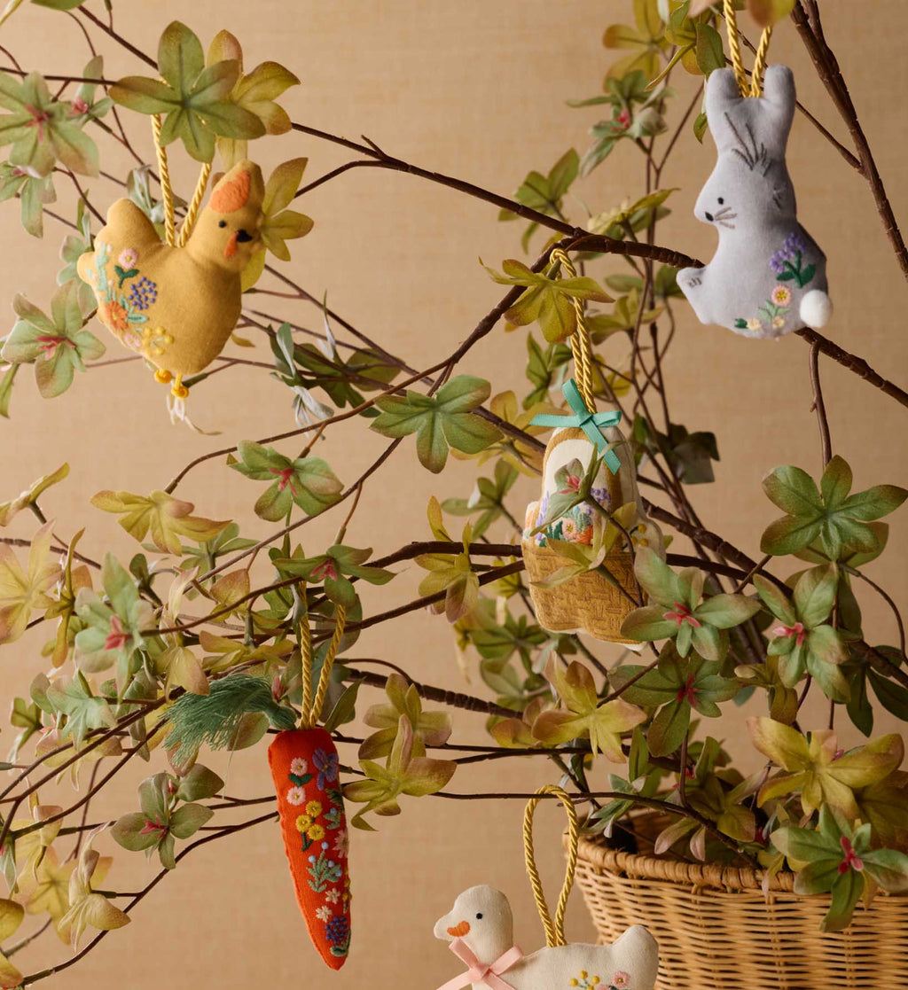 Decorative Easter ornaments hanging on a branch with leaves and flowers.