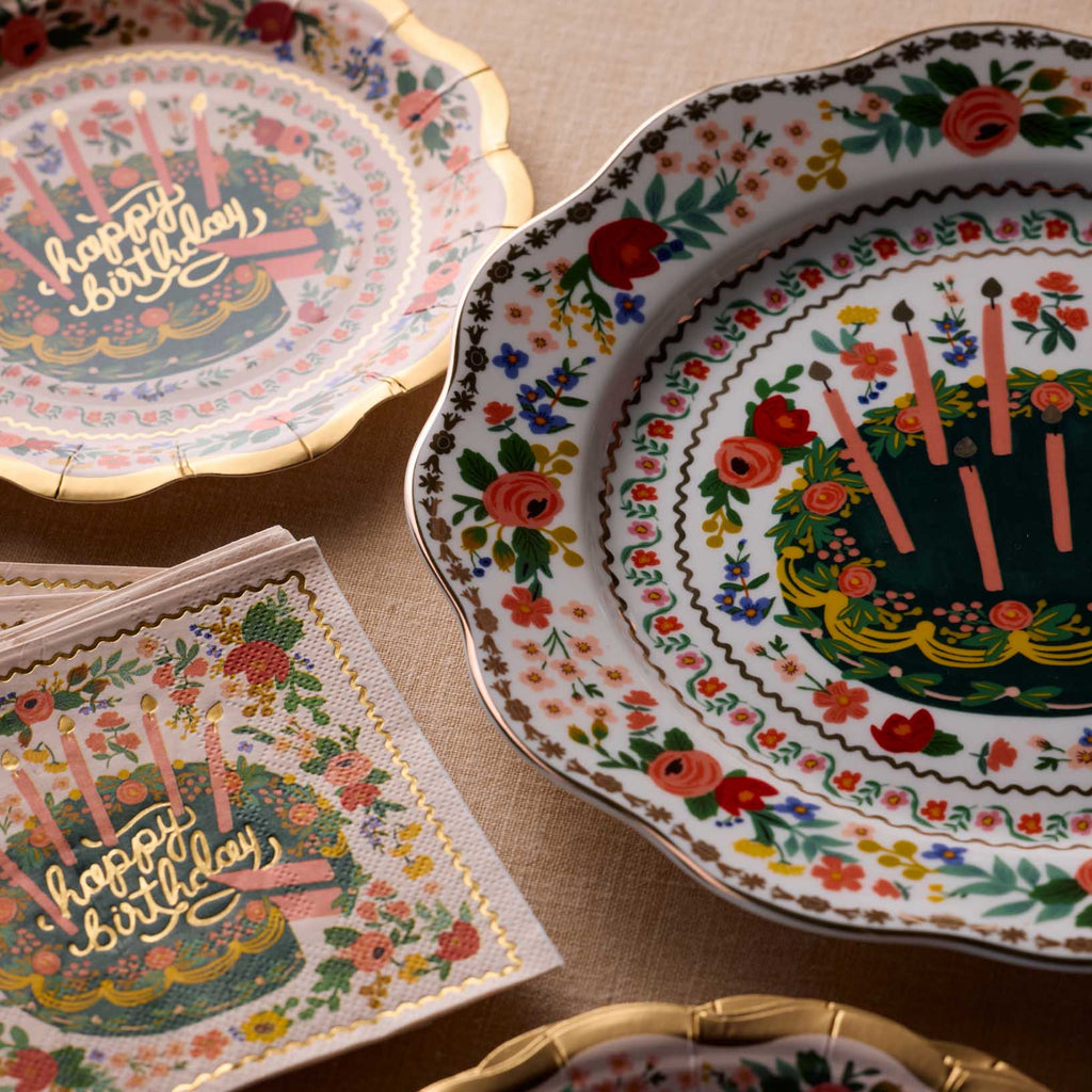 Decorative birthday-themed plates and napkins with floral and cake designs on a beige surface.