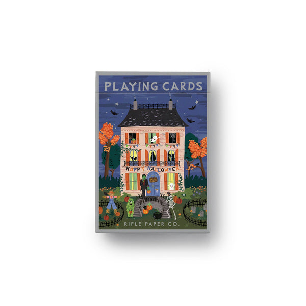 A boxed deck of playing cards from Rifle Paper Co. The front of the box features a whimsical, folk-art style illustration of a house at night with colorful trees, a cat, and the text 'PLAYING CARDS' and 'RIFLE PAPER CO.