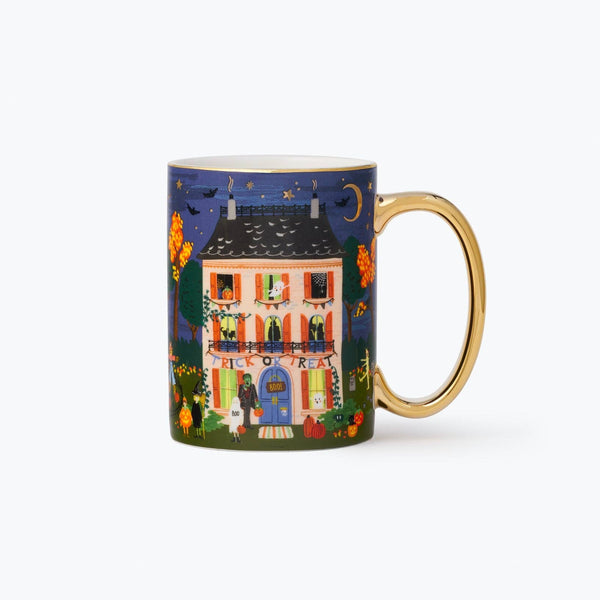 A ceramic mug featuring a colorful illustration of a haunted house at night under a starry sky, with a shiny gold handle, set against a plain white background.