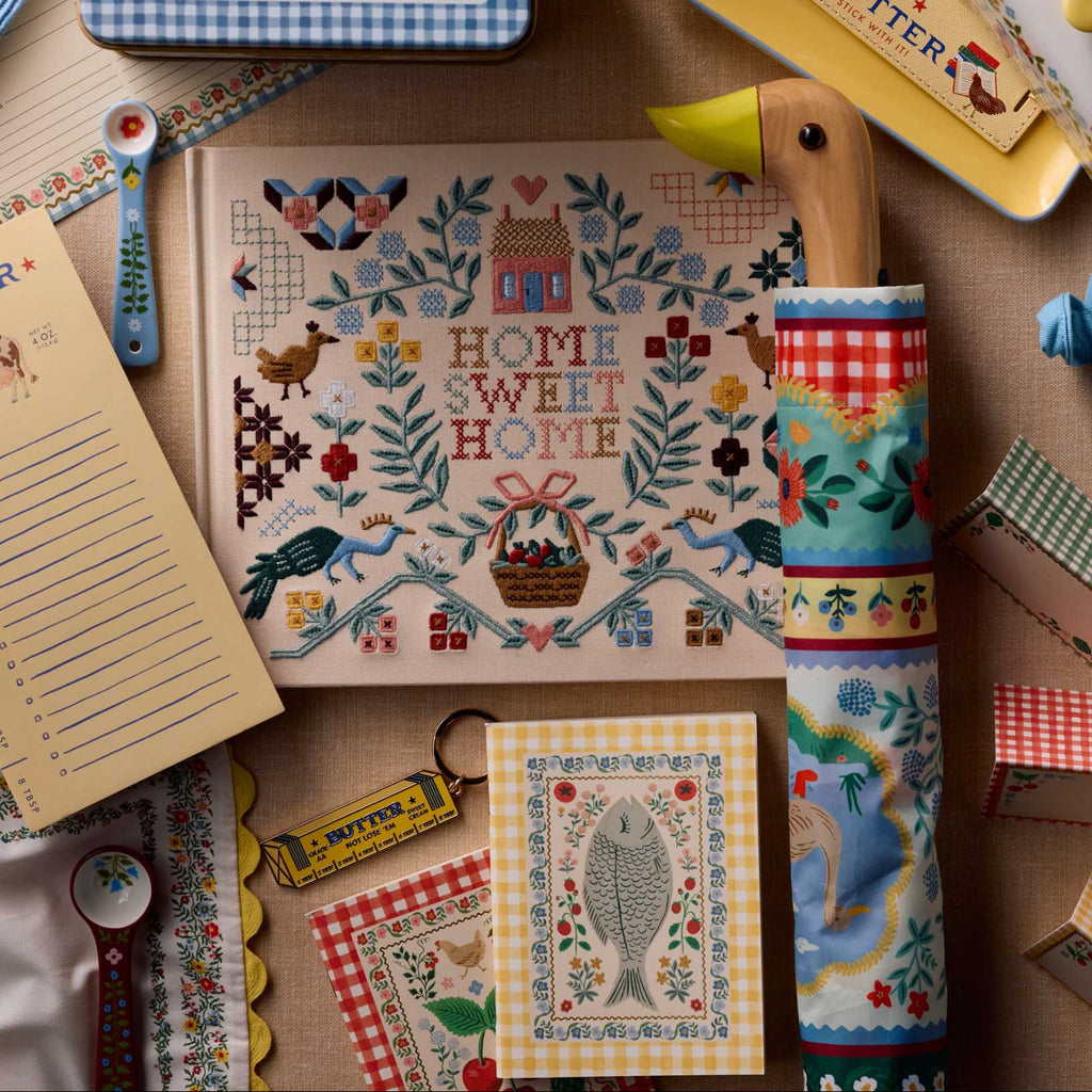 Collection of decorative kitchen items including a cross-stitched 'Home Sweet Home' sign, a patterned towel, and various small kitchen accessories on a wooden surface.