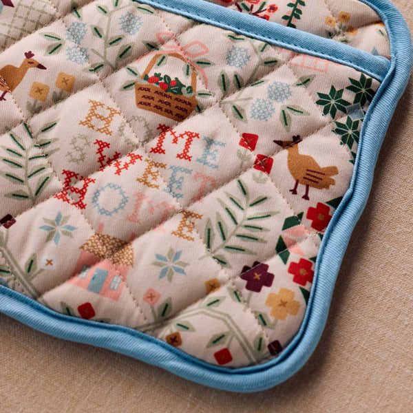 Quilted pot holder with embroidered designs on a beige surface