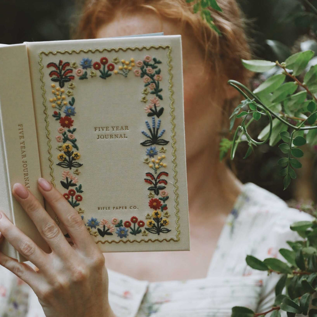 Person holding a 'Five Year Journal' with floral design, surrounded by greenery