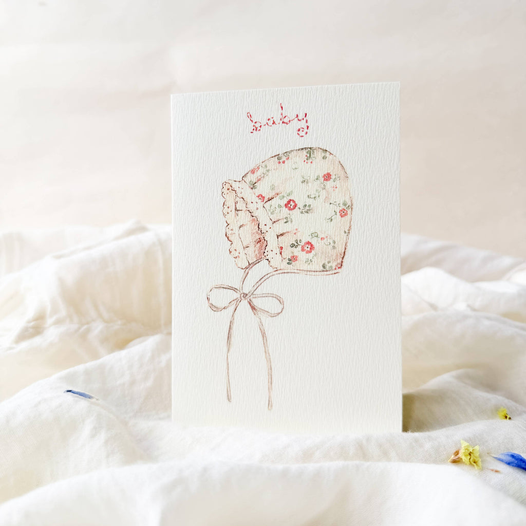 Floral baby bonnet illustration on a white card with a soft white background