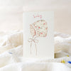 Floral baby bonnet illustration on a white card with a soft white background