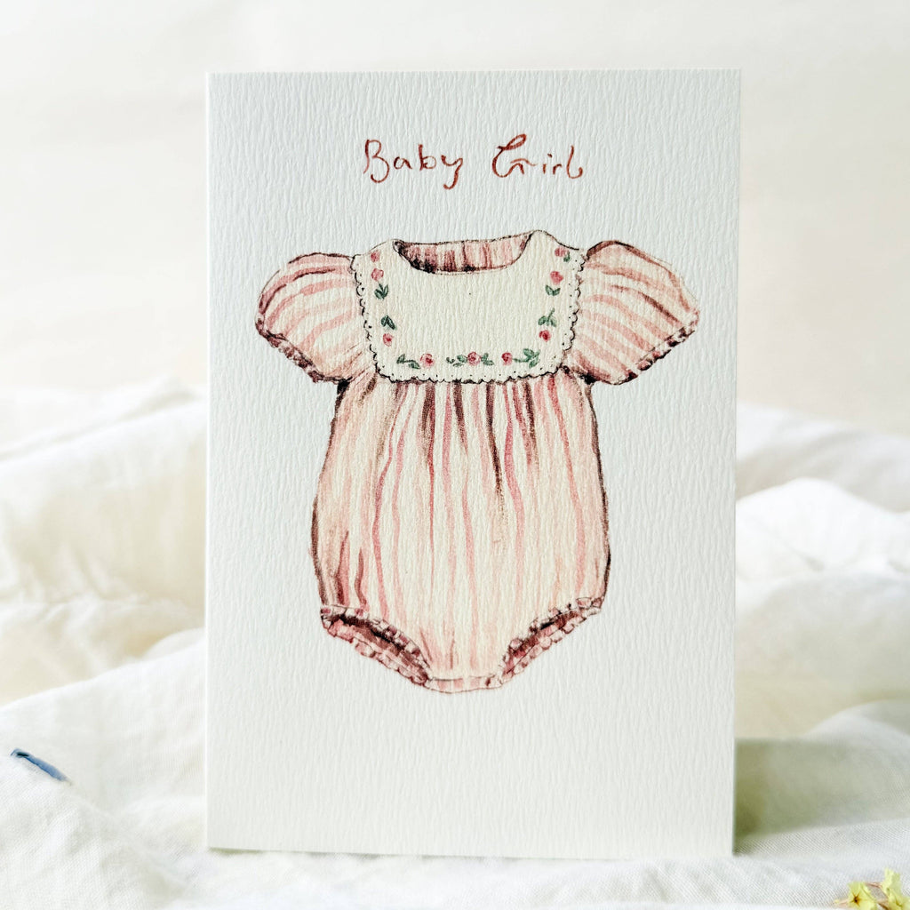 Illustration of a baby girl romper on a textured card with 'Baby Girl' text.