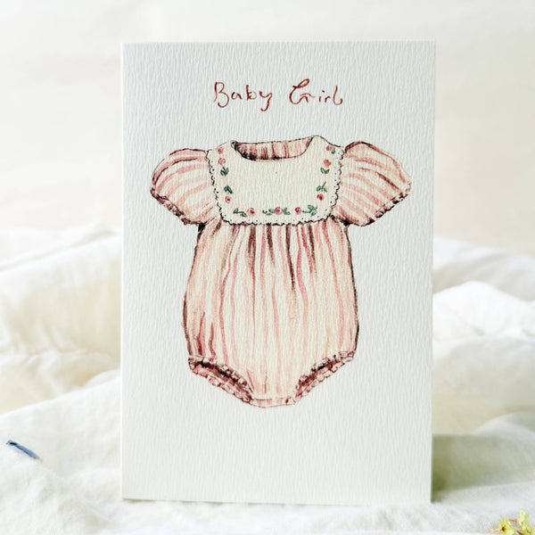 Illustration of a baby girl romper on a textured card with 'Baby Girl' text.