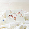 Card with 'big hugs' text and teddy bear illustrations on a soft white background