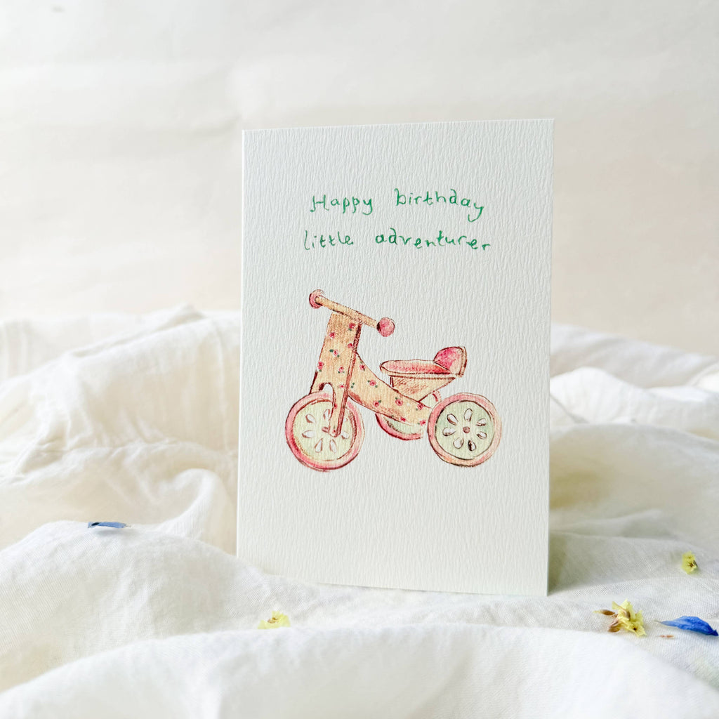 Greeting card with a bicycle illustration and 'Happy birthday little adventurer' text on a white surface.