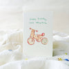 Greeting card with a child's bicycle illustration and 'Happy birthday little adventurer' text on a white surface.