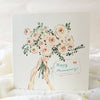 Card with a hand holding a bouquet of flowers and 'Happy Anniversary' text on a soft white background.