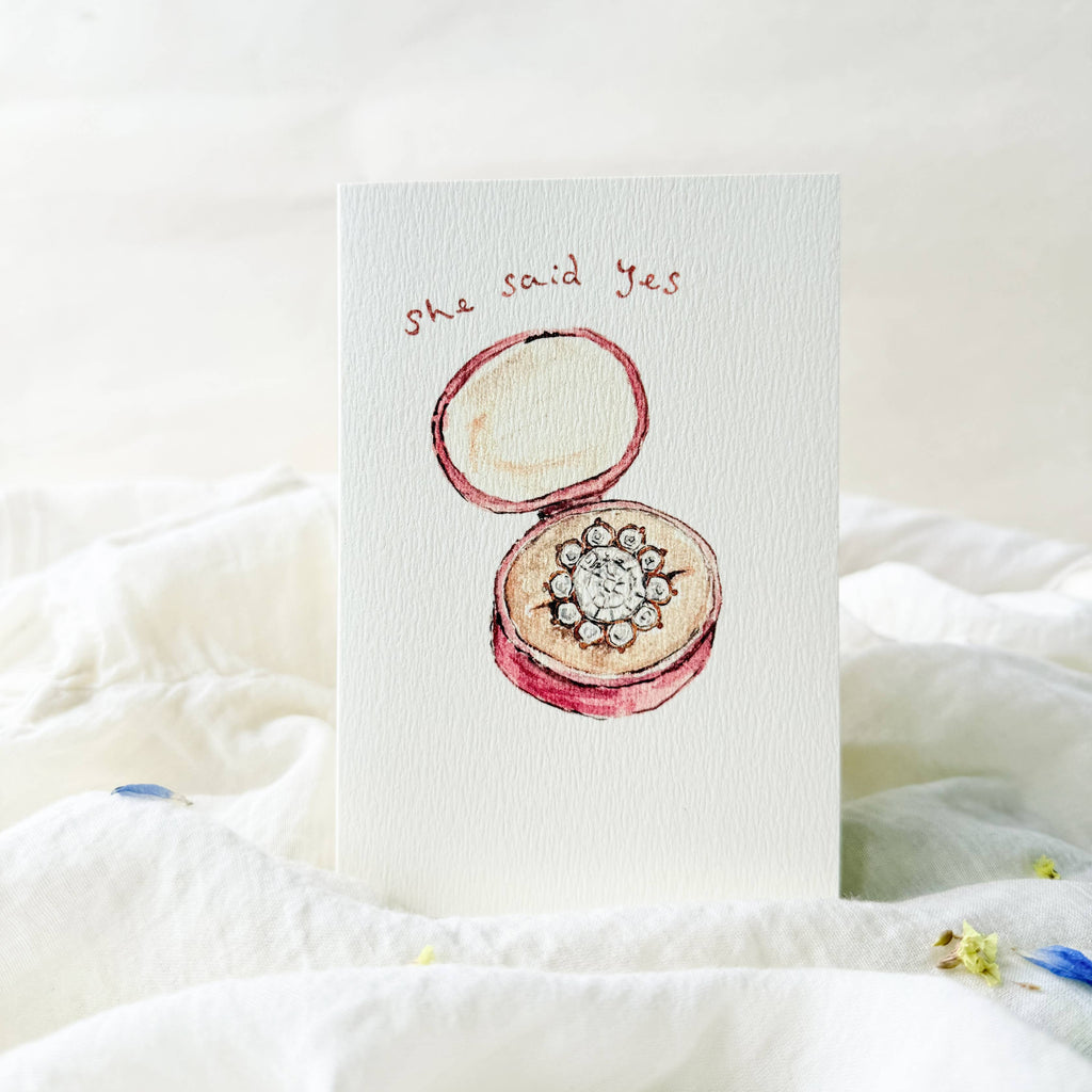 Card with an illustration of a ring box and 'She said yes' text on a white background