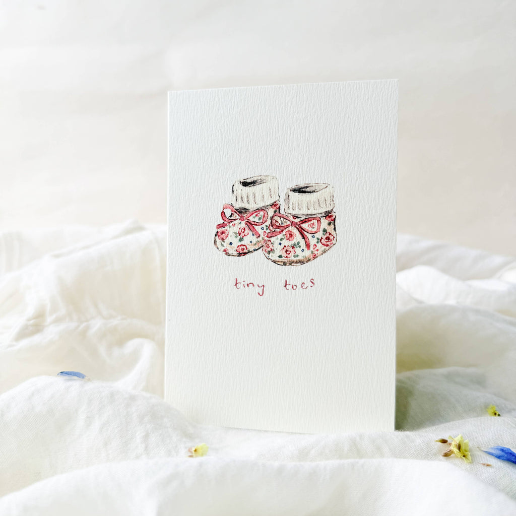 Card with floral baby booties illustration and 'tiny feet' text on a white background