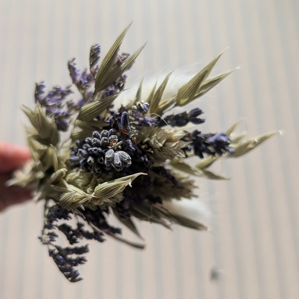 Bouquet of dried lavender and greenery held by a hand against a neutral background