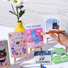 Collection of greeting cards with cat illustrations on a white brick wall background