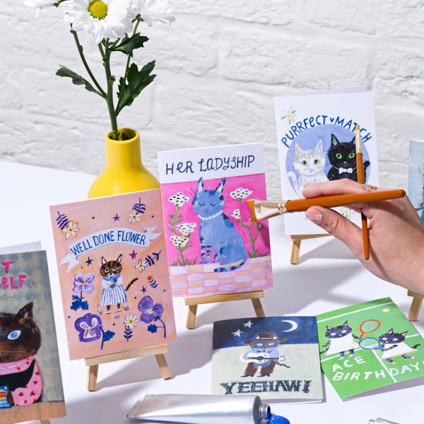 Collection of greeting cards with cat illustrations on a white brick wall background
