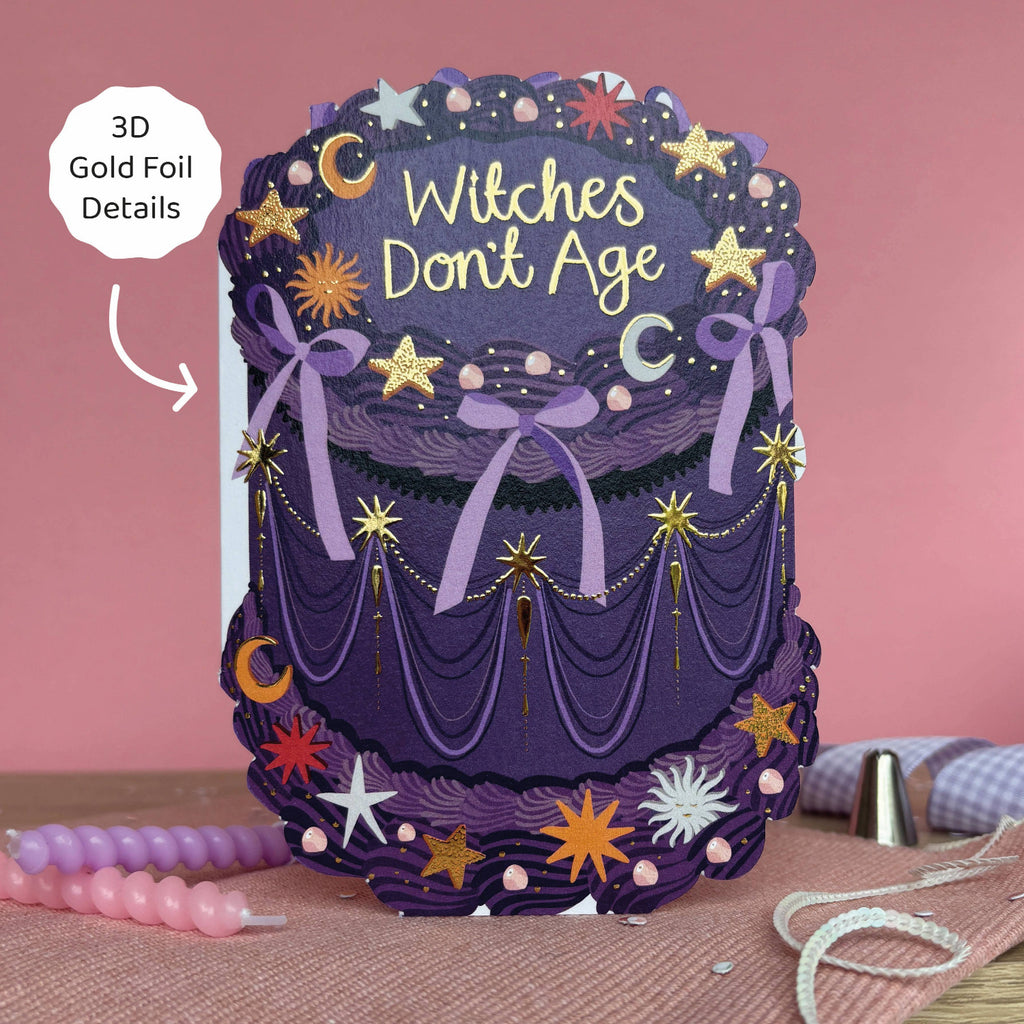 Decorative cake with 'Witches Don't Age' text and gold foil details on a pink background