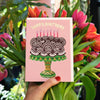 Hand holding a birthday card with a cake illustration surrounded by flowers.