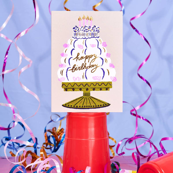 Birthday card with cake illustration and 'Happy Birthday' text, surrounded by colorful party streamers on a blue background.