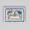 Greeting card with a drawing of a birthday cake on a table, framed by decorative elements on a gray background.