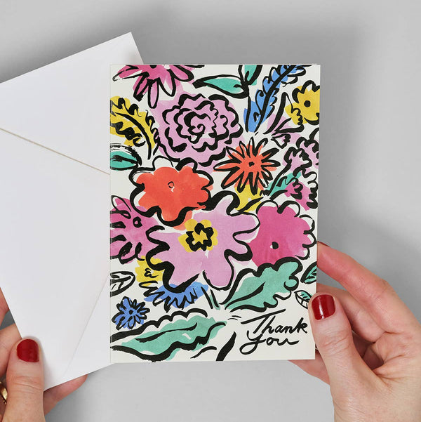 Colorful floral card with 'Thank you' text held by hands against a gray background