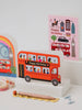Card with a red double-decker bus design and 'Happy Birthday' text, surrounded by other cards and stationery items.