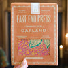 Hand holding a box labeled 'East End Press Garland' with decorative elements.