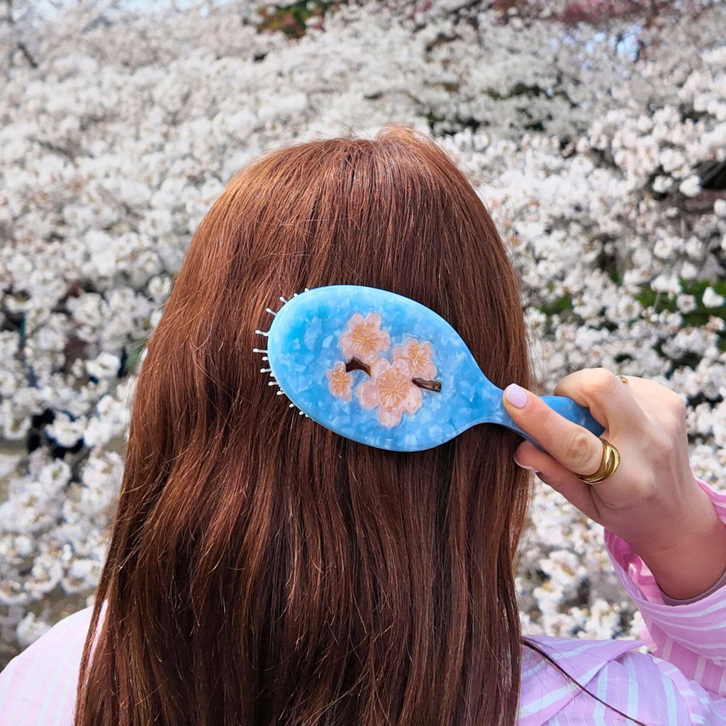 Person brushing their hair with a blue brush against a cherry blossom background