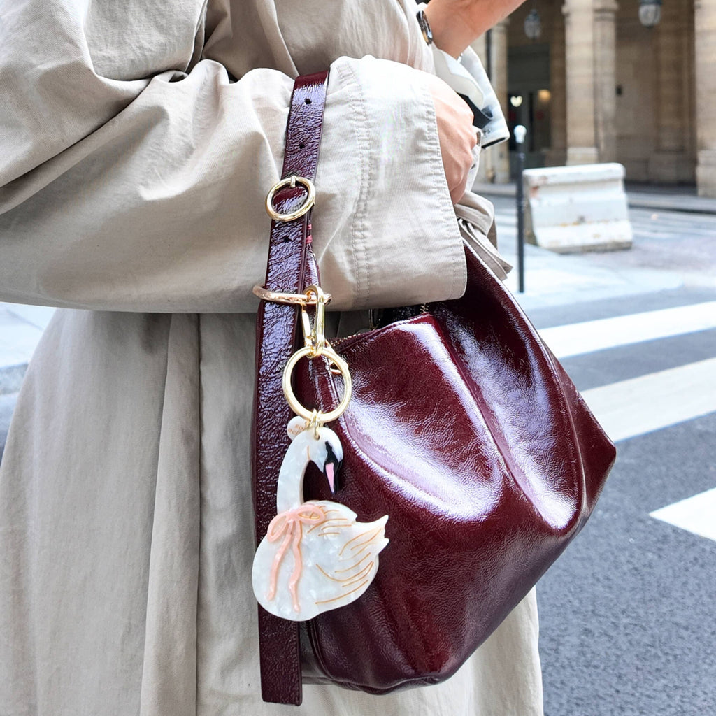 Person holding a burgundy handbag with a decorative charm, walking on a city street.