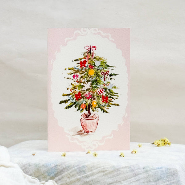 Christmas card with a watercolor illustration of a Christmas tree on a white surface.