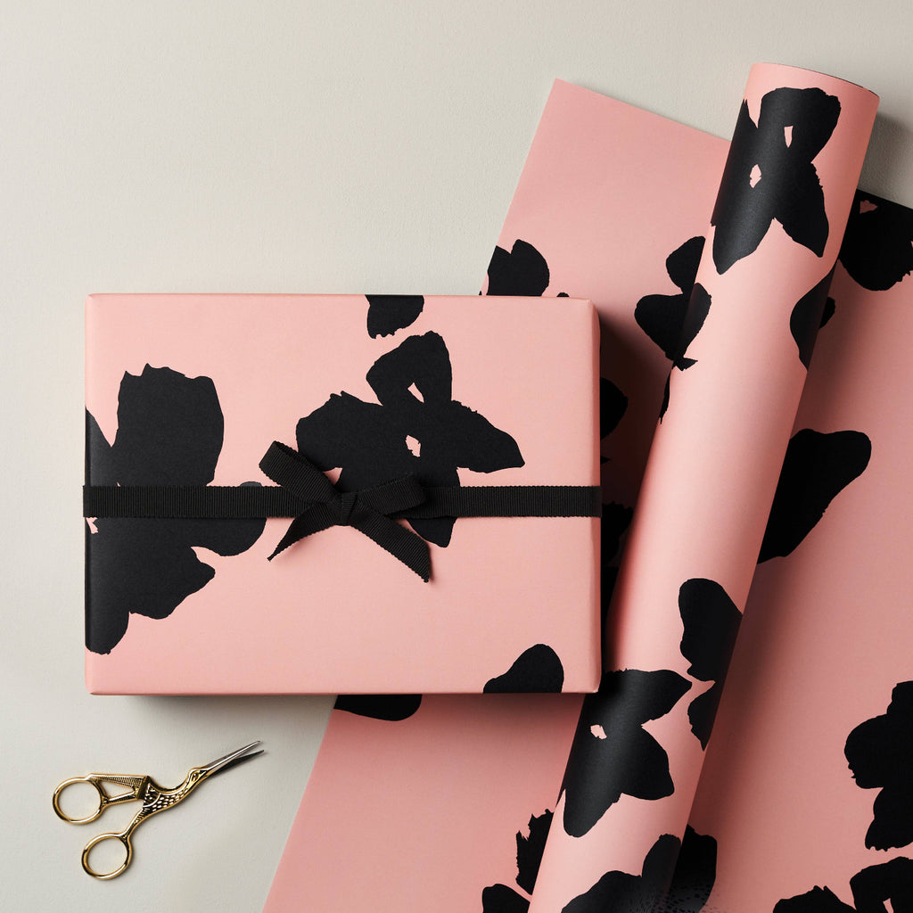 Pink gift box and wrapping paper with black floral patterns on a light gray background