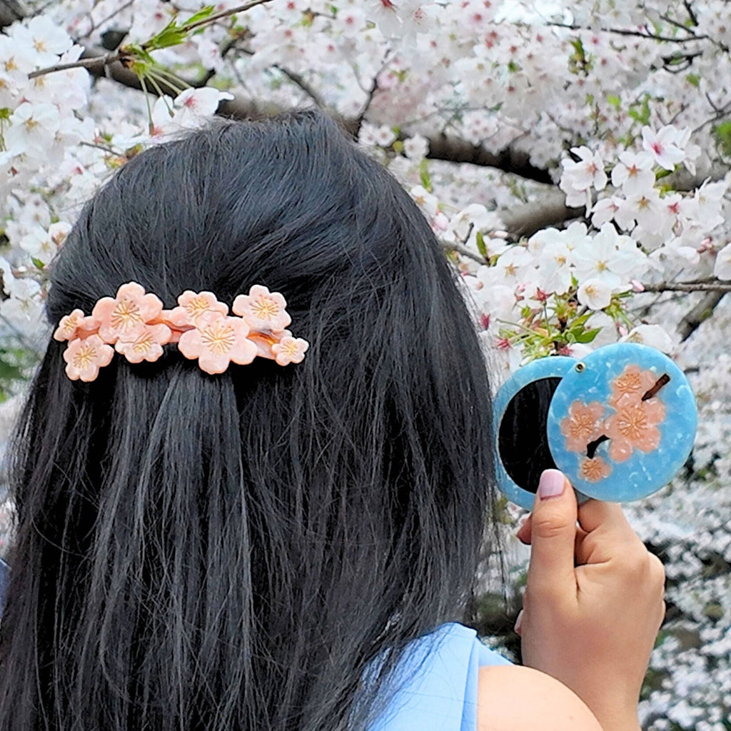 Person with a floral hair clip in front of cherry blossom trees