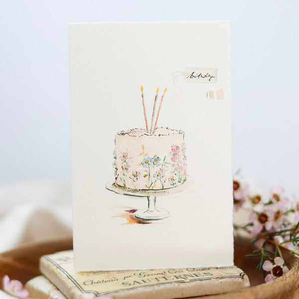 Notebook with floral cake illustration and candles on a wooden surface