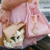 Person holding a pink handbag with a floral bouquet and keychain, blurred background