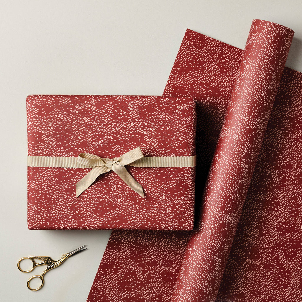 Red patterned gift box with a bow and matching wrapping paper on a light background