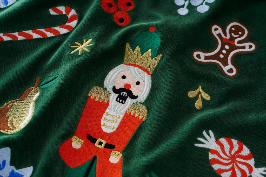Embroidered nutcracker design on a green fabric background with Christmas elements.