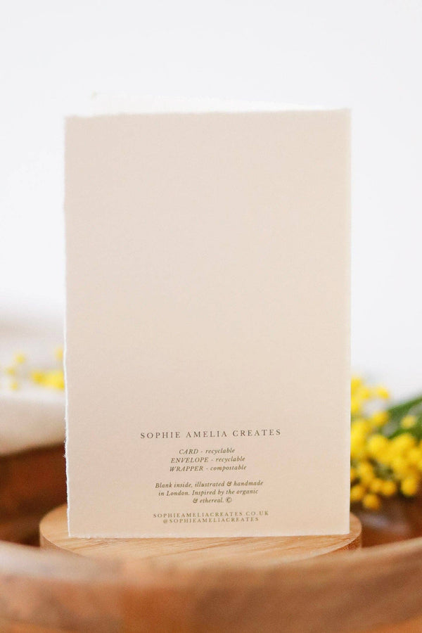 Beige card with text on a wooden stand with yellow flowers in the background