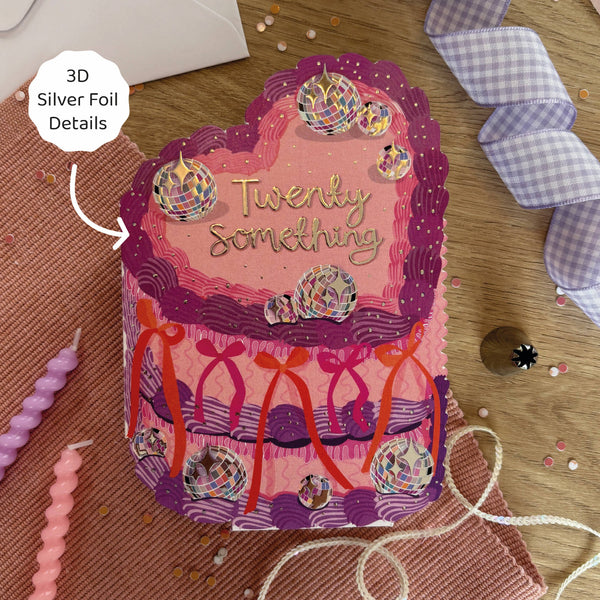 Decorative birthday card with 'Twenty Something' text and 3D silver foil details on a wooden surface.
