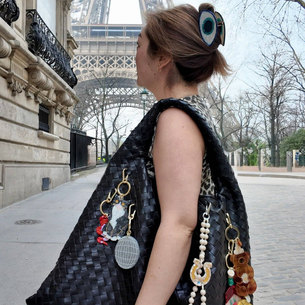 Woman with a large black handbag featuring various accessories in front of the Eiffel Tower.