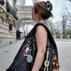 Woman with a large black handbag featuring various accessories in front of the Eiffel Tower.