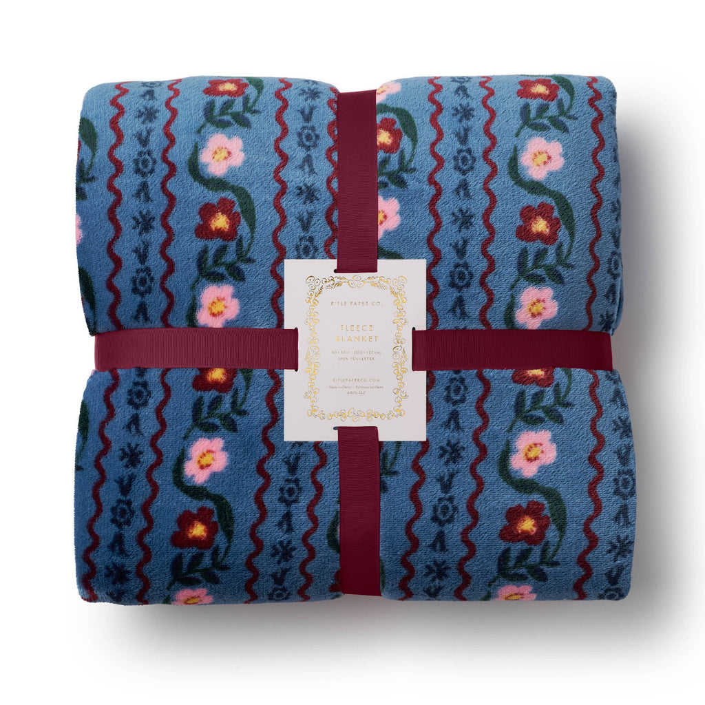 Folded blue blanket with floral patterns and a red ribbon on a white background
