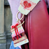 Decorative keychain with heart design attached to a pink bag.